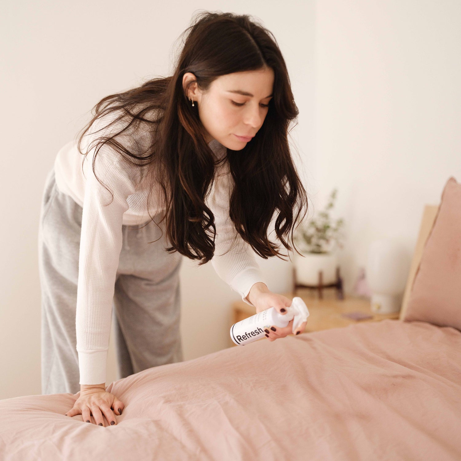A woman spraying Jason Markk Refresh Spray on her bed to instantly neutralize any odors.