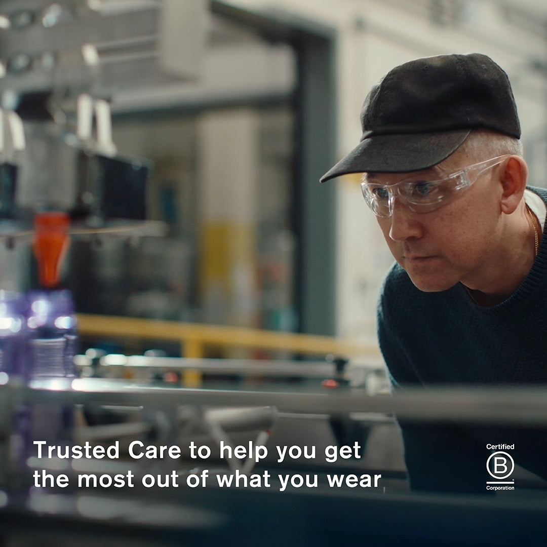 Jason Markk focused and wearing safety goggles and a black cap closely inspects a production line in our manufacturing facility. A Certified B Corporation badge appears in the bottom right corner. Text overlay reads: "Trusted Care to help you get the most out of what you wear."