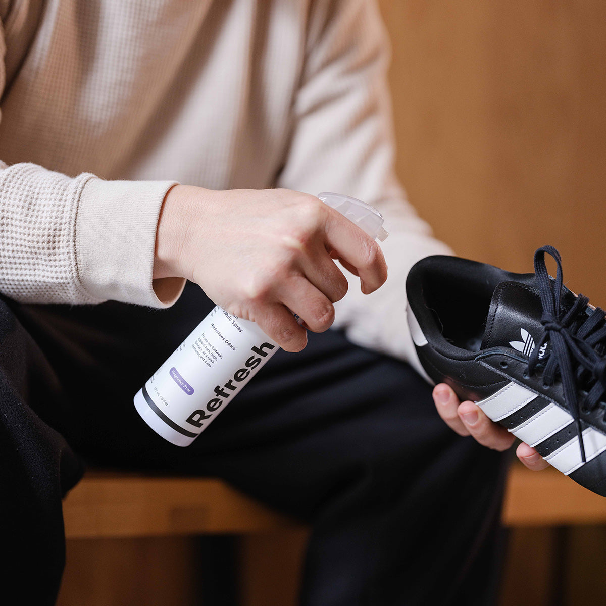 A photo of a man spraying Jason Markk Fragrance Free Refresh Spray into a pair of Adidias Shoes