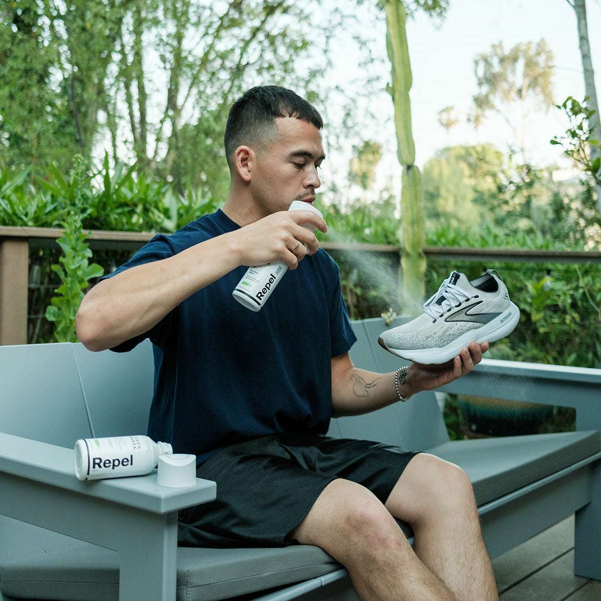 Man spraying Brooks Running shoes with Jason Mark Repel Spray with Refill bottle sitting next to him.