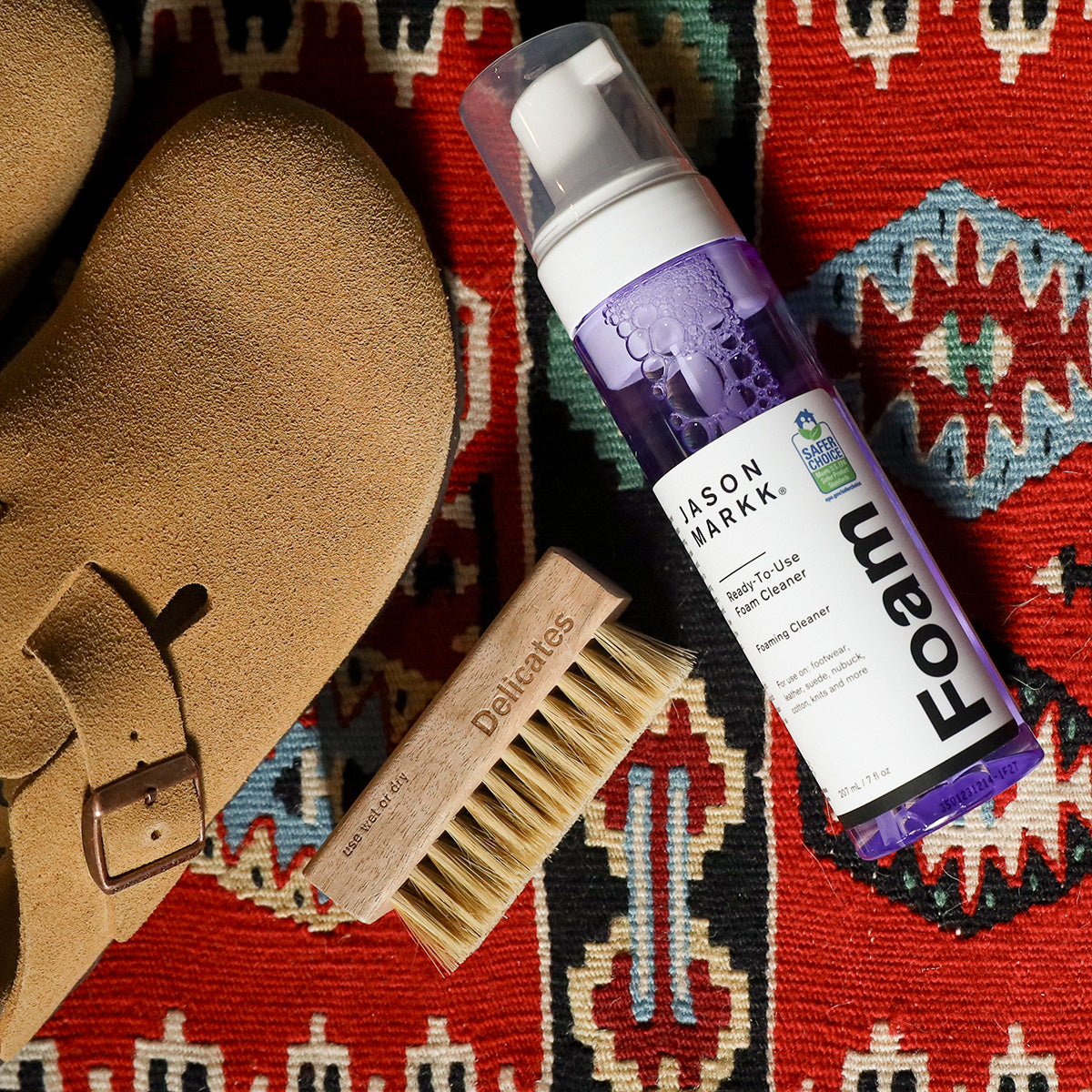 Birkenstock Bostons sitting on a decorative rug next to a Delicate Brush and Ready to Use Foam