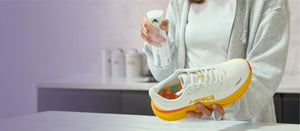 Person spraying a white Hoka sneaker with orange accents using a Repel. bottle.