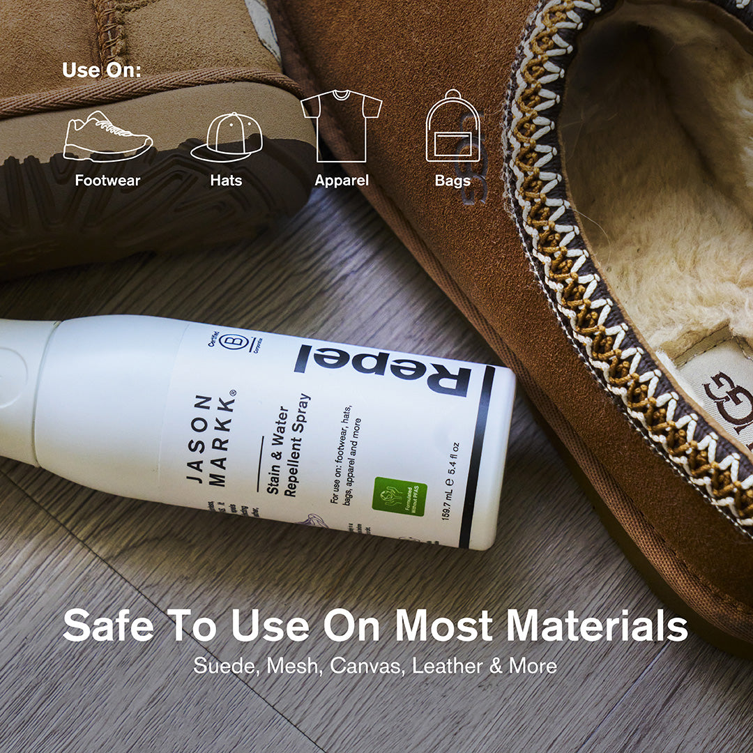 A 5.4 fl oz bottle of Jason Markk Repel Stain and Water Repellent Spray lying on a wood floor next to a pair of tan suede UGG moccasins with shearling lining. Icons along the top indicate compatible item types: Footwear, Hats, Apparel, and Bags. Text overlay reads: "Safe To Use On Most Materials – Suede, Mesh, Canvas, Leather & More."