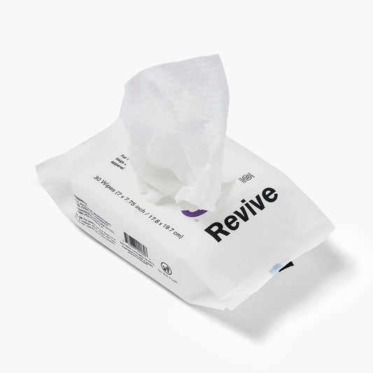 Jason Markk Essential 30pk Quick Wipes cleaning wipes package, 30 count (7x7.75 inch / 17.8x19.7 cm), shown open with a wipe pulled out. White flexible pouch with bold black "Revive" branding and purple logo. Labeled for bags, apparel, and accessories. Includes barcode and Do Not Flush symbol. White background.