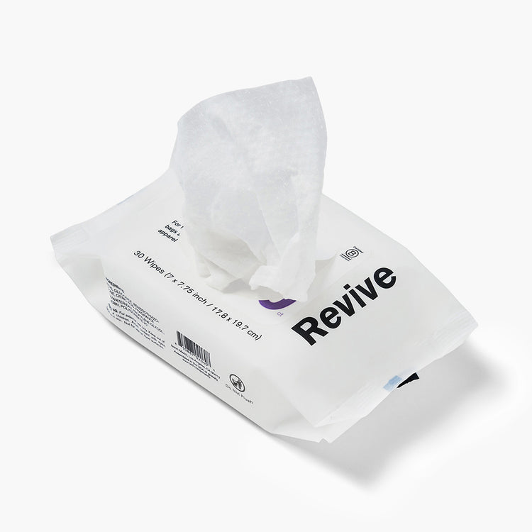 Jason Markk Essential 30pk Quick Wipes cleaning wipes package, 30 count (7x7.75 inch / 17.8x19.7 cm), shown open with a wipe pulled out. White flexible pouch with bold black "Revive" branding and purple logo. Labeled for bags, apparel, and accessories. Includes barcode and Do Not Flush symbol. White background.