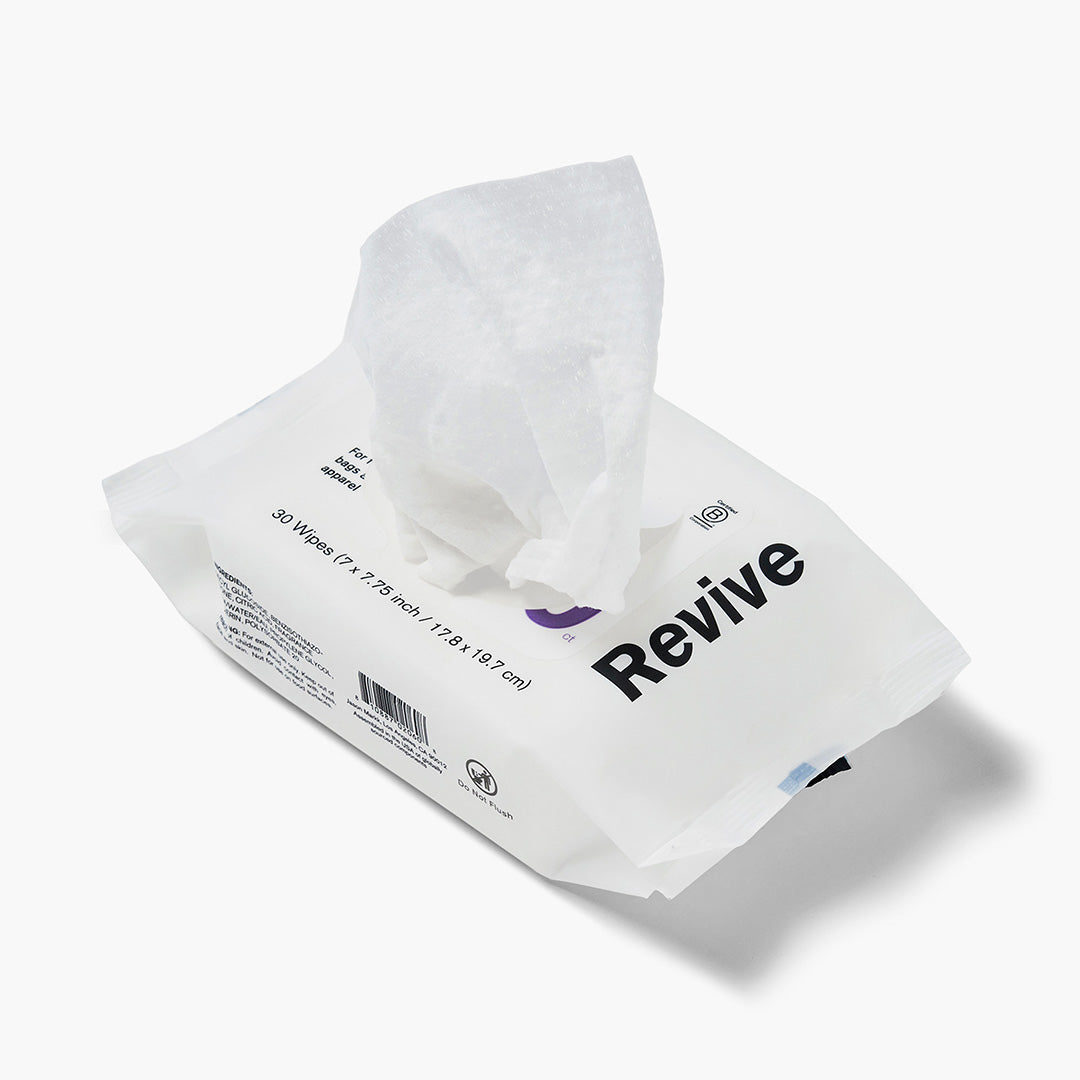 Jason Markk Essential 30pk Quick Wipes cleaning wipes package, 30 count (7x7.75 inch / 17.8x19.7 cm), shown open with a wipe pulled out. White flexible pouch with bold black "Revive" branding and purple logo. Labeled for bags, apparel, and accessories. Includes barcode and Do Not Flush symbol. White background.