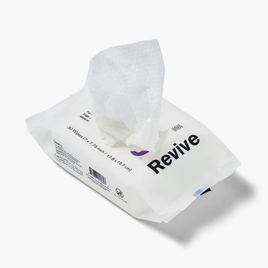 Jason Markk Essential 30pk Quick Wipes cleaning wipes package, 30 count (7x7.75 inch / 17.8x19.7 cm), shown open with a wipe pulled out. White flexible pouch with bold black "Revive" branding and purple logo. Labeled for bags, apparel, and accessories. Includes barcode and Do Not Flush symbol. White background.