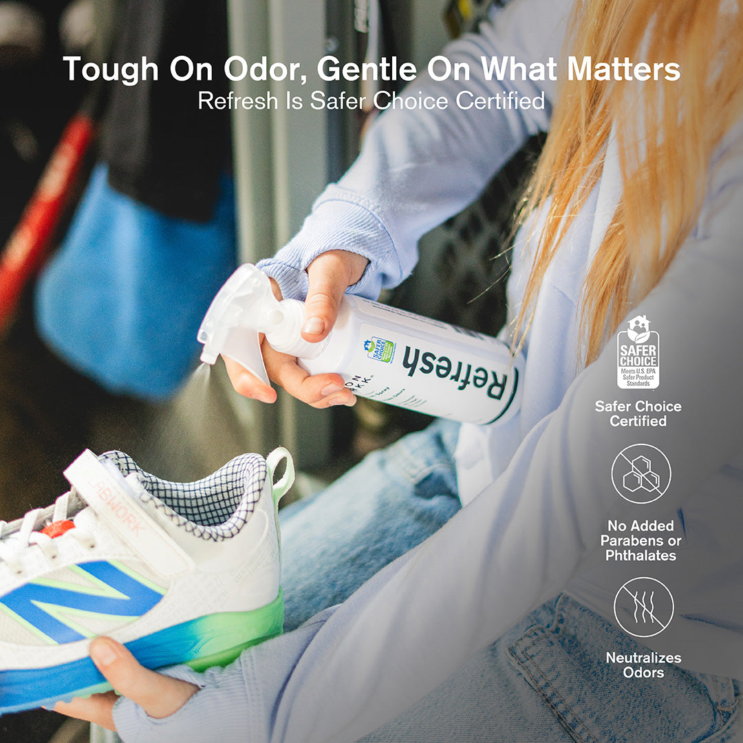 A person in a light blue hoodie and jeans spraying Jason Markk Refresh odor neutralizing spray into a white, blue, and green New Balance sneaker near a locker. Three feature icons on the right highlight: Safer Choice Certified (meets U.S. EPA Safer Product Standards), No Added Parabens or Phthalates, and Neutralizes Odors. Text overlay reads: "Tough On Odor, Gentle On What Matters – Refresh Is Safer Choice Certified."