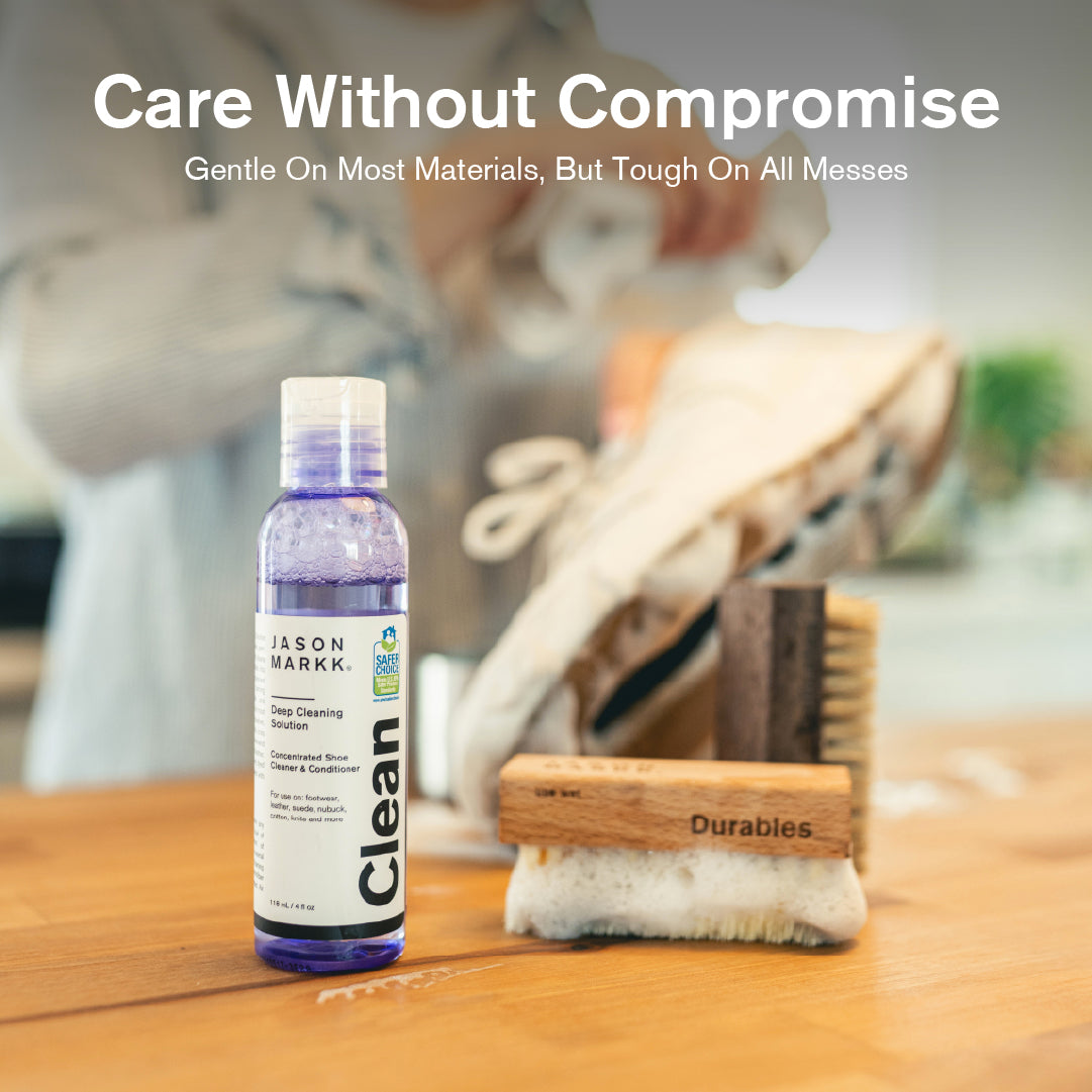 Bottle of Jason Markk Deep Cleaning Solution with a Durables Brush on a wooden surface, with text 'Care Without Compromise'.