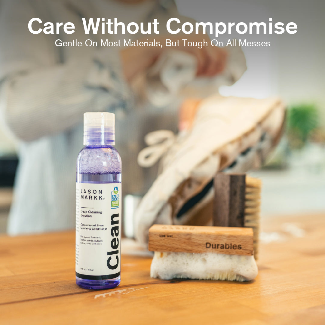 Bottle of Jason Markk Deep Cleaning Solution with a Durables Brush on a wooden surface, with text 'Care Without Compromise'.