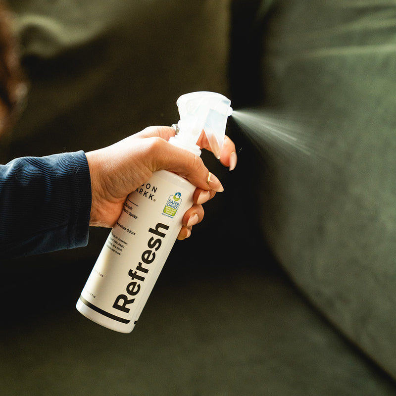 Close-up of hand spraying Jason Markk Refresh shoe deodorizer onto a surface. Fine mist application designed to eliminate odors in shoes, sneakers, and everyday items. Easy-to-use spray for keeping footwear fresh, clean, and odor-free as part of a daily shoe care routine.