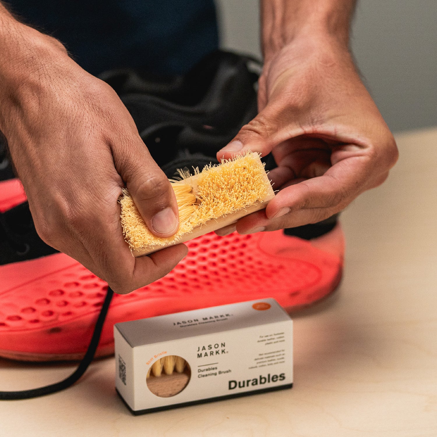 FINGERS BRUSHING THROUGH THE BRISTLES OF A JASON MARKK DURABLES BRUSH IN FRONT OF A PAIR OF ADIDAS AE1 SHOES