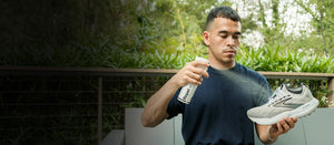 Man holding a sneaker and spraying Repel outdoors with greenery in the background