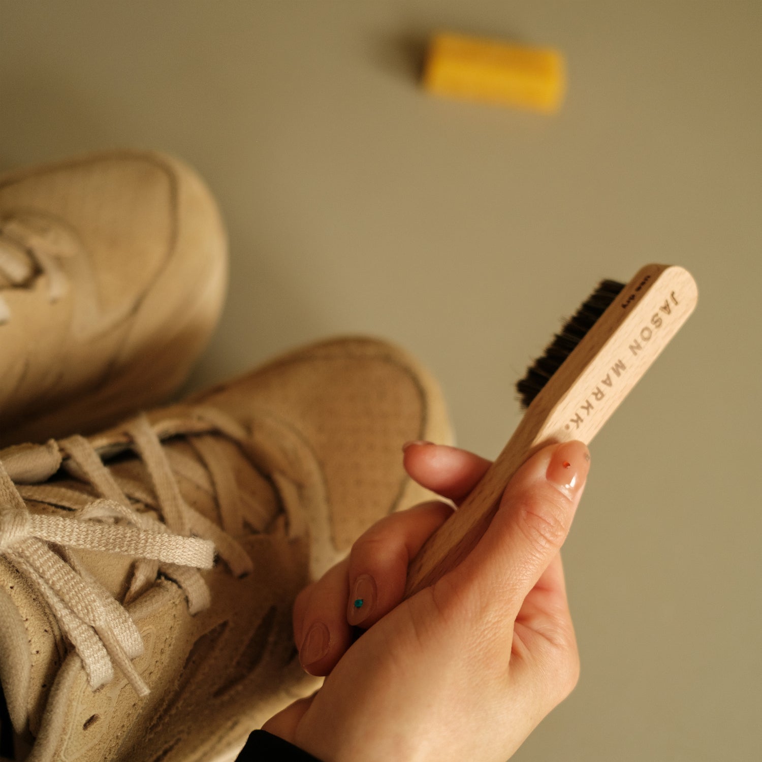 A JASON MARKK SUEDE CLEANING BRUSH HELD ABOVE A PAIR OF HOKA CLIFTON SHOES