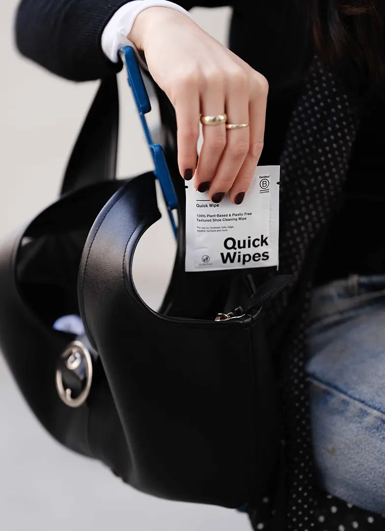 Person holding a black bag with a packet of Quick Wipes in hand.