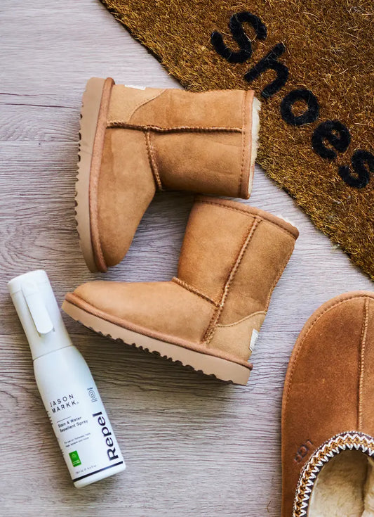 Tan suede boots with a bottle of Repel Spray on a wooden floor, next to a doormat with 'Shoes' text.