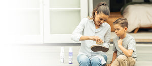 A mom and her son sit together on a porch as she scrubs a shoe with a Jason Markk Delicates Brush. Jason Markk Repel Stain & Water Repellent Spray and Ready-To-Use Foam Cleaner bottles are displayed in the foreground. Jason Markk premium shoe care products safe for the whole family. Enjoy 20% off bundles for Mothers Day.