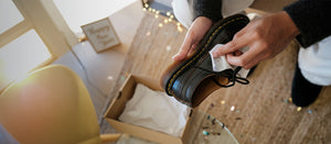 Person cleaning a black leather shoe with a Jason Markk Quick Wipes over a wooden floor.