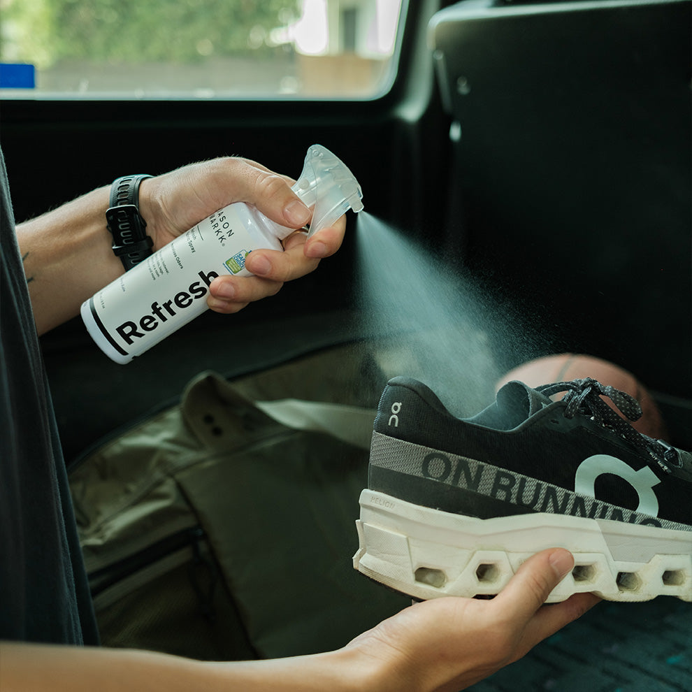 Person using a Refresh Spray on a pair of running shoes inside a vehicle.