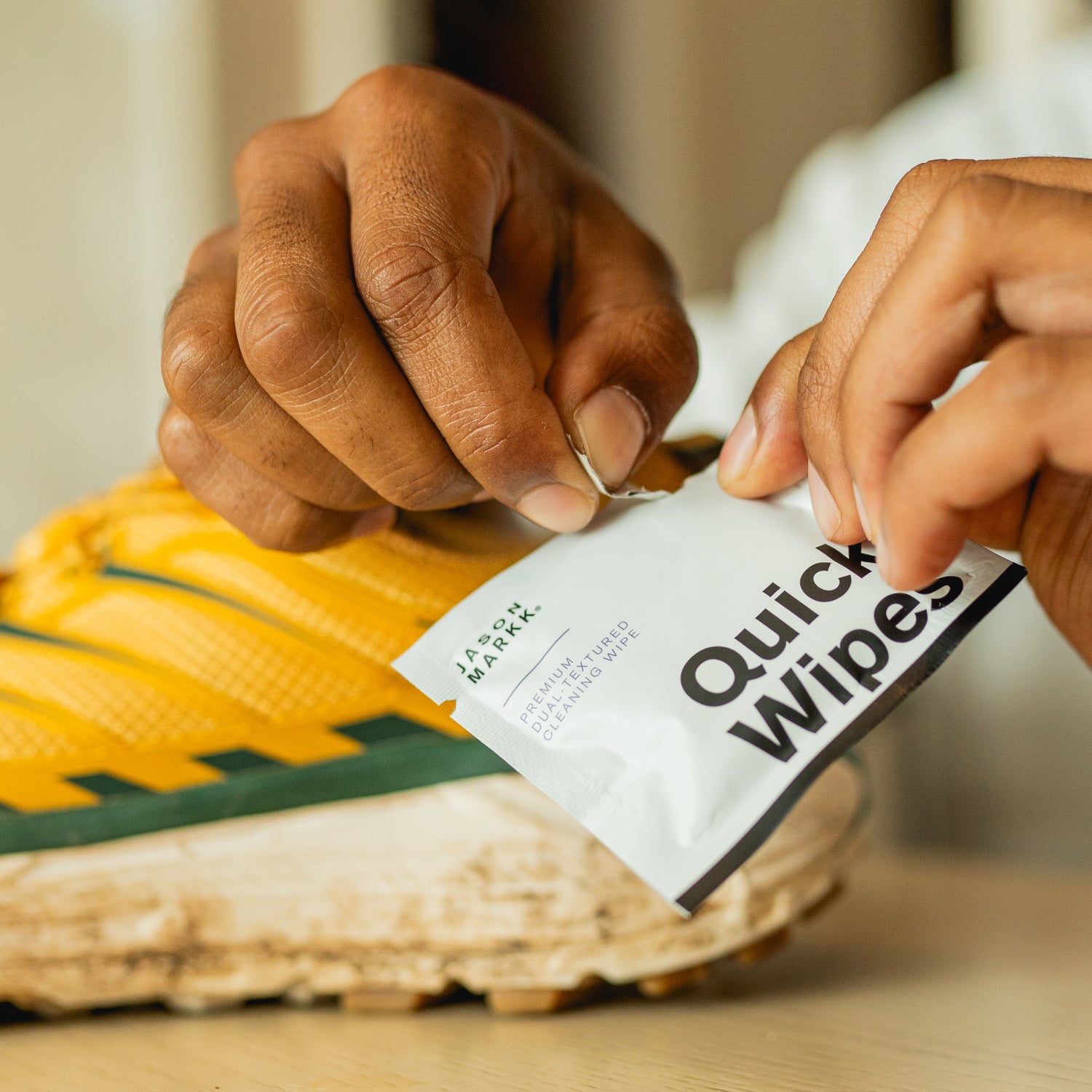 JASON MARKK QUICK WIPE FOIL PACKAGING BEING OPENED IN FRONT OF A YELLOW HOKA RUNNING SHOE