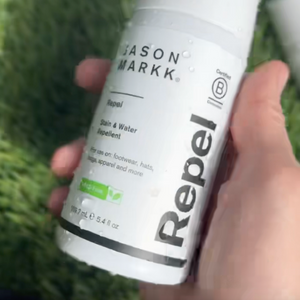 Hand holding a bottle of Jason Markk Repel stain and water repellent against a grassy background