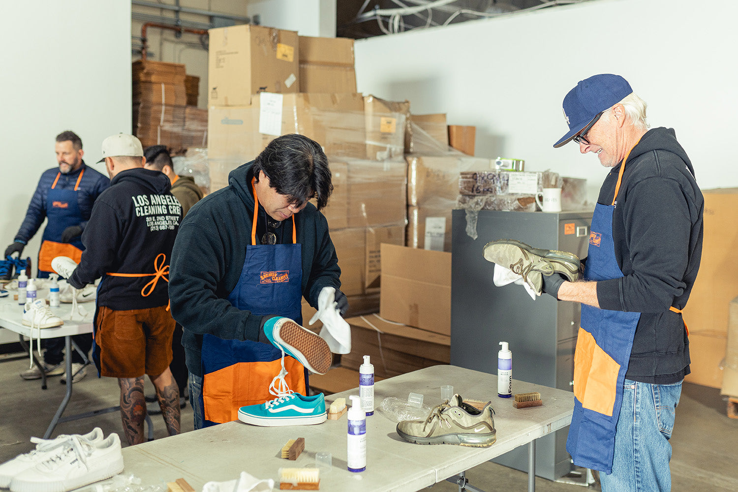 Jason Markk Team Members in a warehouse setting with boxes and tables, cleaning a shoes to be donated.