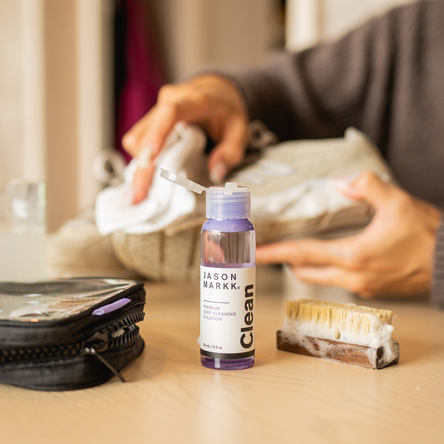 A JASON MARKK TRAVEL KIT IN FRONT OF A PERSON LEANING A PAIR OF NEW BALANCE IN THE BACKGROUND