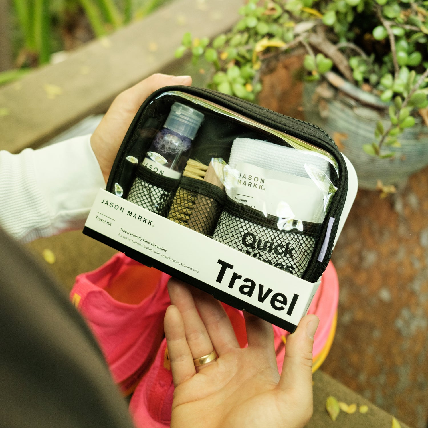 A PACKAGED JASON MARKK TRAVEL KIT HELD ABOVE A PAIR OF NIKE RUNNING SHOES