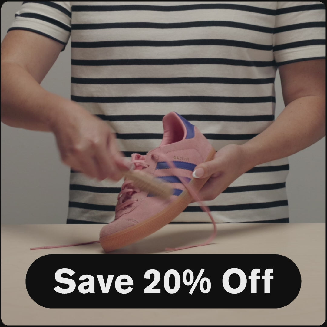 Video: Person in a black and white striped shirt cleaning a pink Adidas Gazelle sneaker with purple stripes and a gum sole, with Suede Care Bundle while held over a neutral surface. Text overlay reads: "Save 20% Off." 16-second product video demonstrating sneaker care and handling for the Jason Markk Suede Care Bundle promotion.