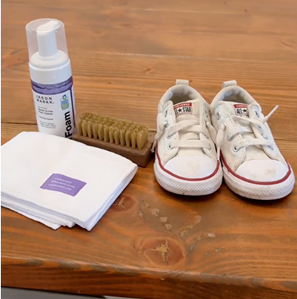 White sneakers with red soles on a wooden surface, accompanied by RTU Foam, Delicates Brush, and Microfiber Towel.